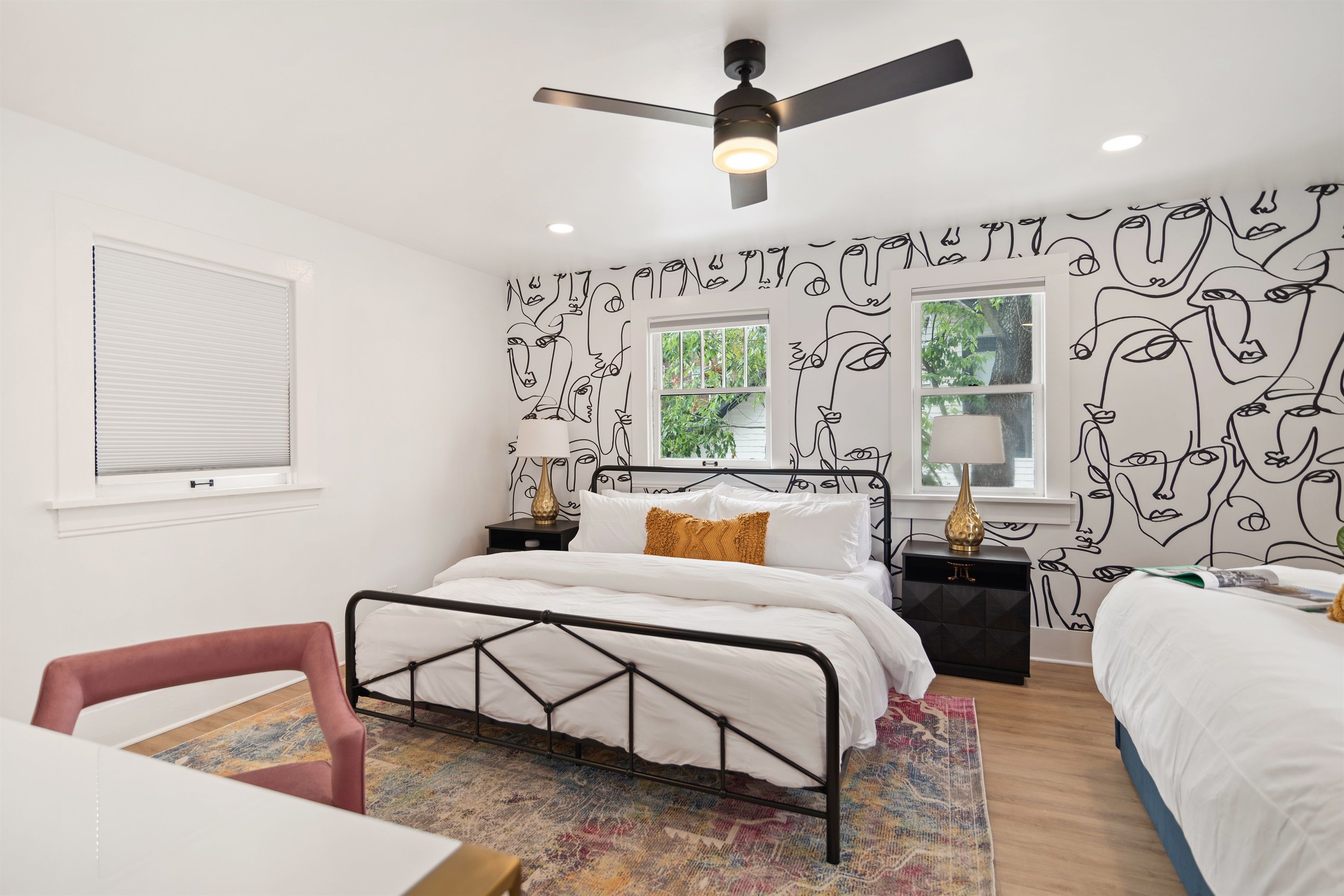 Une chambre à coucher comprenant un lit, une chaise, une table de chevet, une lampe et un ventilateur de plafond.