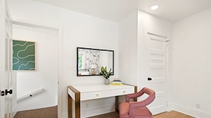 A room with a white desk, a pink chair, a framed abstract art piece, and a door with a handle.