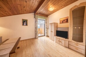 A room with wooden flooring, a television on a wooden cabinet, a table, and a door leading outside.