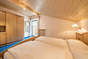 A bedroom with two beds, wooden wardrobe, and a window with curtains.