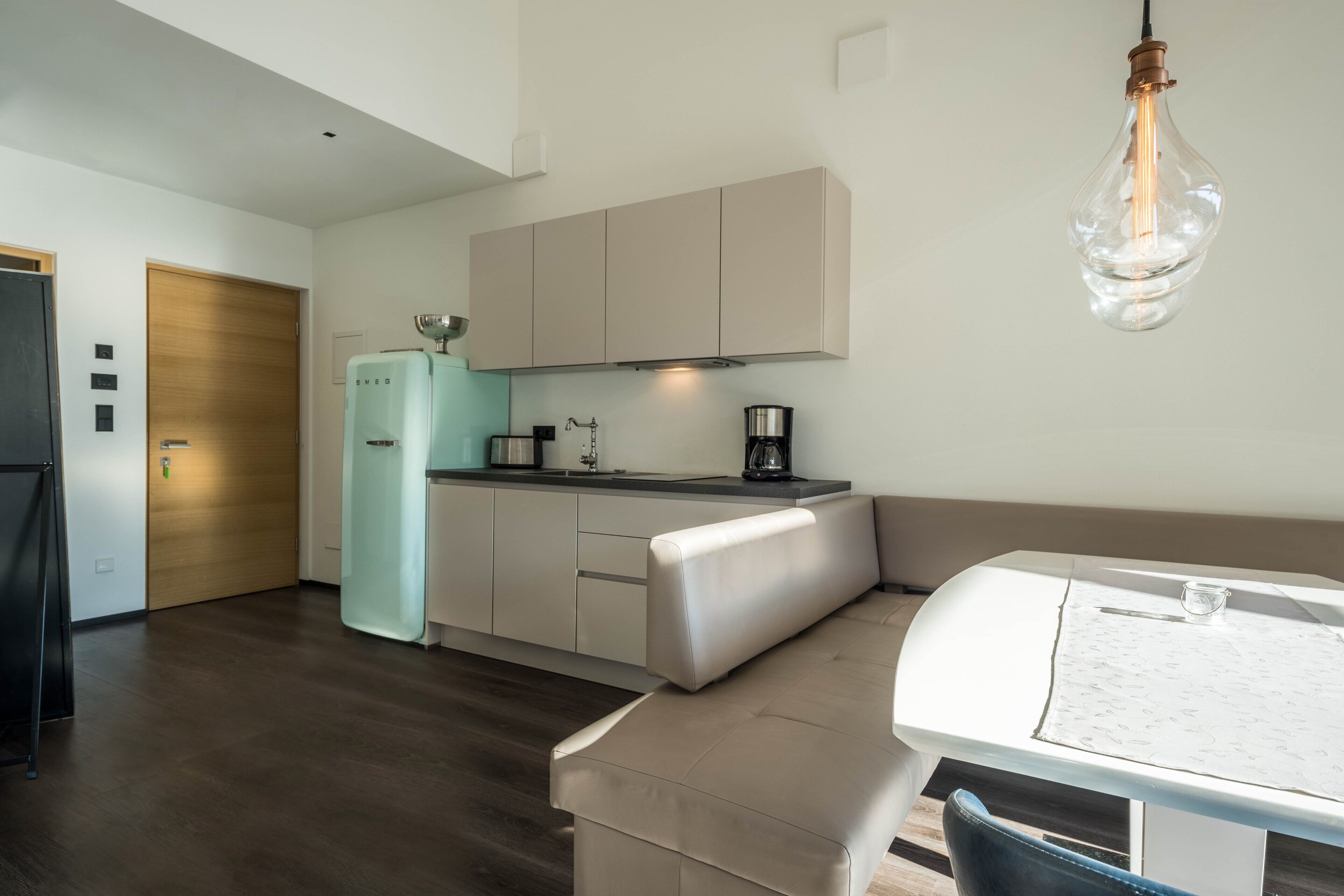 A modern kitchen with a refrigerator, stove, and coffee maker. There is a dining area with a table and chairs.