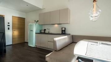 A modern kitchen with a refrigerator, stove, and coffee maker. There is a dining area with a table and chairs.