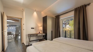 Habitación de hotel con cama, escritorio, lámpara, ventana con cortinas y vista a un edificio.