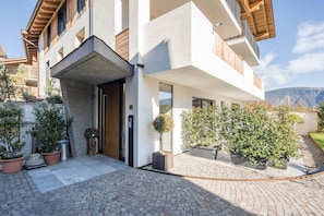Un bâtiment moderne doté d’une façade en pierre, de grandes fenêtres et d’un espace d’entrée pavé agrémenté de plantes en pot.