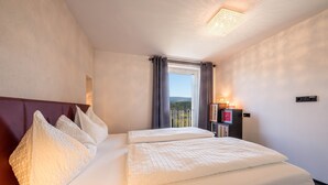 A hotel room with a large bed, a bedside table with a lamp, a window with curtains, and a view of the outdoors.