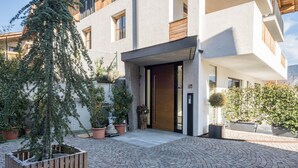 A modern building with a paved courtyard, potted plants, and a wooden fence.