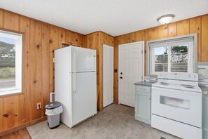 Cocina compacta con paredes de madera, un refrigerador, una estufa y un cubo de basura.