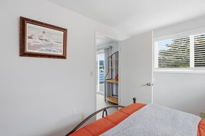 Un dormitorio con cama, ventana con persianas, puerta que da a un baño y un cuadro en la pared.