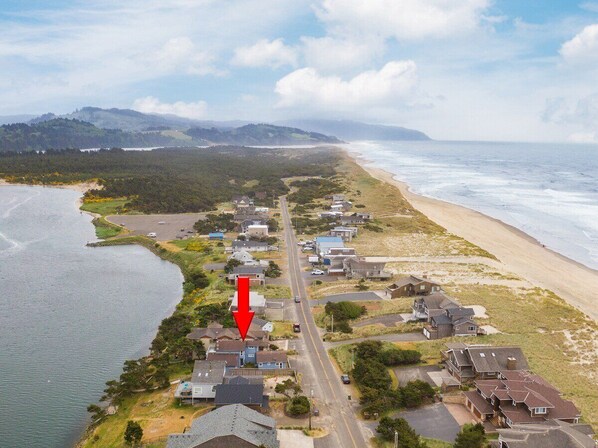 An aerial view of a coastal residential area with houses along the beach, a road, and a body of water. - #155 Nestucca Sunrise · Riverfront, Close to Ocean Beaches, Large Yard (Pacific CIty)