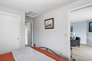Un dormitorio con cama, una puerta, un cuadro en la pared y vistas a otra habitación con un sofá.