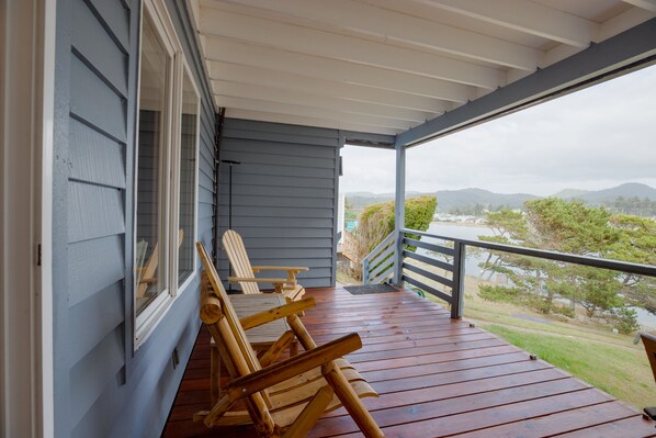 A wooden deck with two Adirondack chairs, a view of a lake, and a mountainous landscape in the distance.