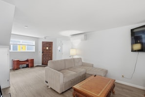 Una sala de estar con un sofá seccional color beige, una mesa de centro de madera y un televisor montado en la pared.