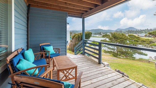 A covered porch with wooden furniture and a view of a lake and mountains. - #155 Nestucca Sunrise · Riverfront, Close to Ocean Beaches, Large Yard (Pacific CIty)