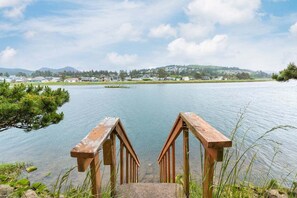 A wooden dock leading into a calm lake with a view of a small town in the distance. - #155 Nestucca Sunrise · Riverfront, Close to Ocean Beaches, Large Yard (Pacific CIty)