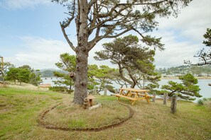 Een picknicktafel en bankje bij een meer, met bomen en een brug in de verte.