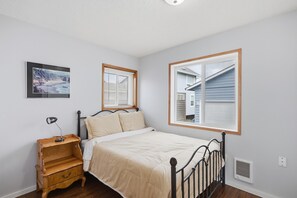 Un dormitorio con cama, mesita de noche, lámpara, ventana con persianas y un cuadro en la pared.