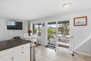 Una cocina moderna con televisor, armarios blancos, encimera de granito y comedor con sillas blancas.