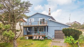 A two-story house with a balcony, a garage, and a small garden area. - #155 Nestucca Sunrise · Riverfront, Close to Ocean Beaches, Large Yard (Pacific CIty)