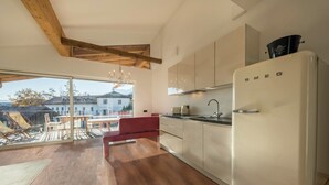 A modern kitchen with a large window, wooden beams, and a red chair. - Apartment "Berg und Tal - Schlosserhaus 31" with Balcony and Mountain View (Tisens Südtirol)
