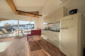 A modern kitchen with a large window, wooden beams, and a red chair.