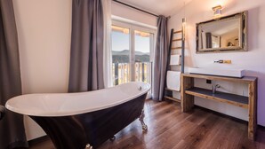 A bathroom with a freestanding bathtub, a vanity with a mirror, and a view of the outdoors. - Apartment "Berg und Tal - Schlosserhaus 31" with Balcony and Mountain View (Tisens Südtirol)