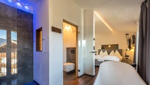 A modern hotel room with a large bed, a small bathroom, and a view of the outdoors. - Apartment "Berg und Tal - Schlosserhaus 31" with Balcony and Mountain View (Tisens Südtirol)