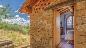 Ein Steinhaus mit Holzdach, ein Eingang zu einem Schlafzimmer mit Bett und Bergblick.