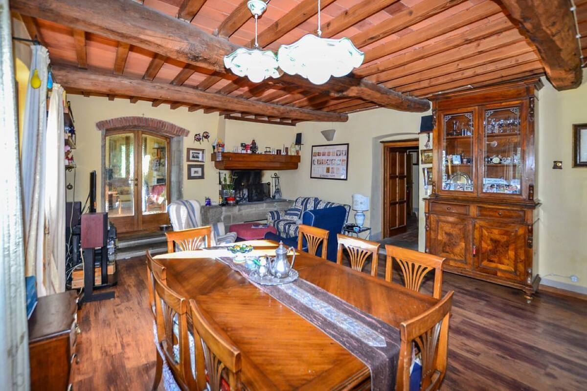 Een ruime eethoek met een houten tafel en stoelen, een open haard en een houten kast met glazen deuren.