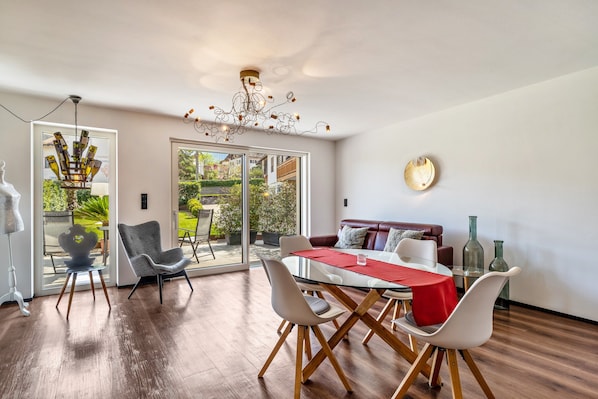 Un espace de salle à manger moderne avec une table en verre, des chaises blanches, un chemin de table rouge et un lustre.
