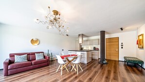 Una sala de estar moderna con un sofá rojo, una mesa de comedor con sillas, una zona de cocina y suelo de madera.