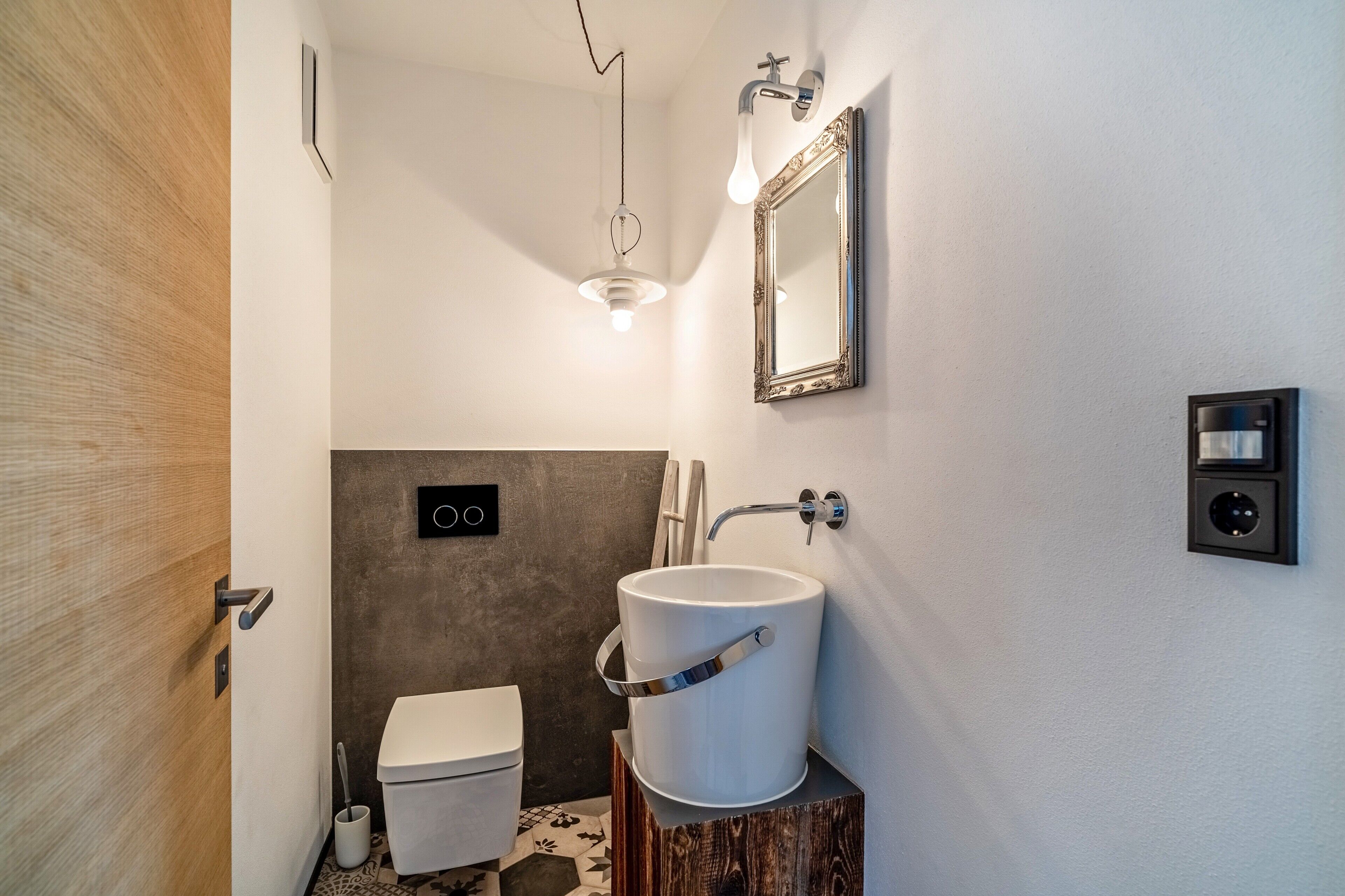 Un baño moderno con lavamanos blanco, un espejo y una lámpara.
