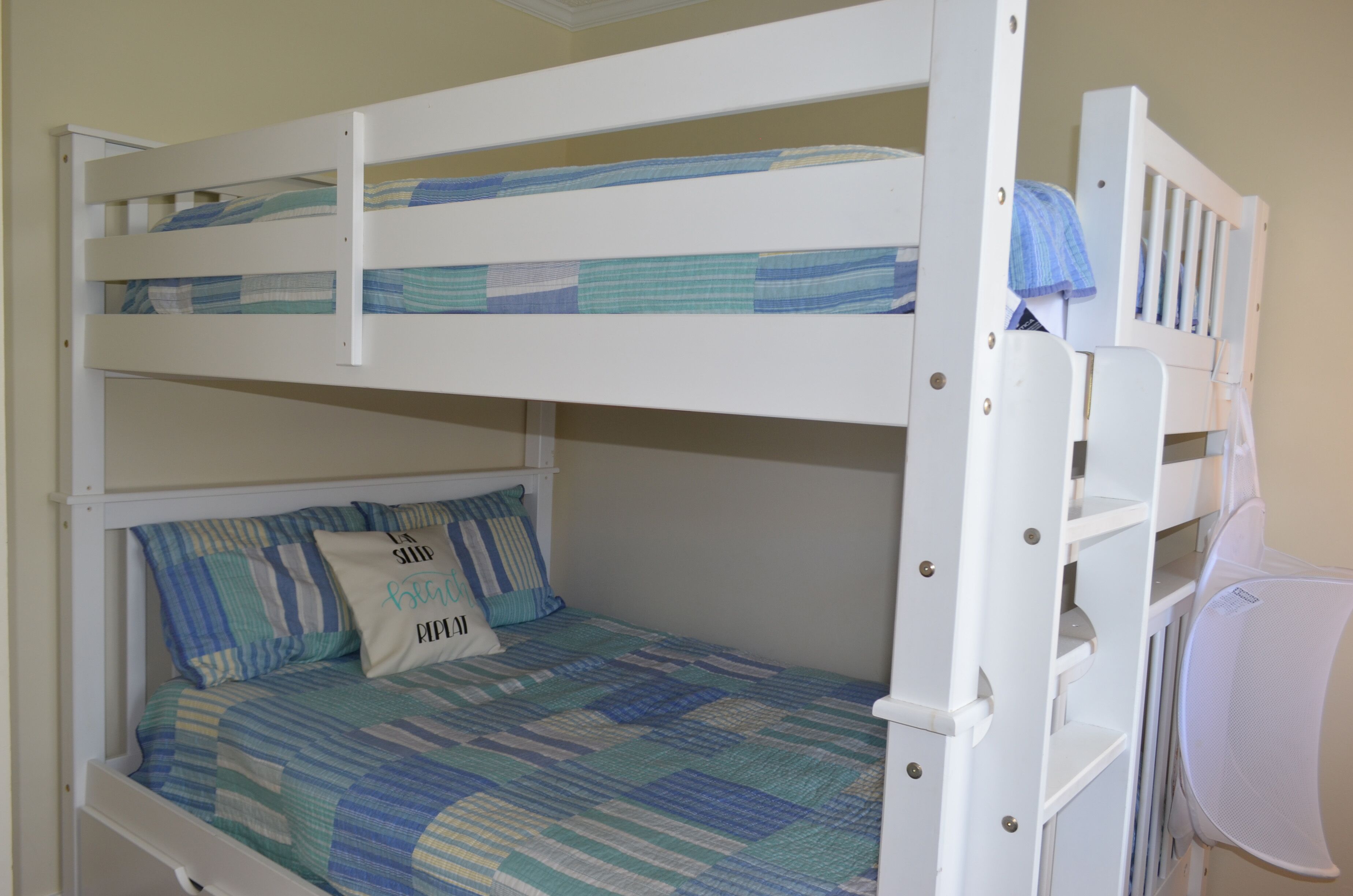 Un lit superposé avec une couvre-lit et des oreillers à rayures bleues et blanches, une tête de lit blanche et une barrière latérale blanche.