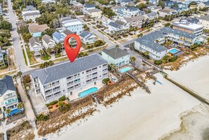 An aerial view of a coastal residential area with a large building featuring multiple balconies, a swimming pool, and a beach access point. - Channel Marker 106 - Oceanfront in Surfside Beach (Surfside Beach)