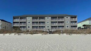 Un immeuble à plusieurs étages doté de balcons, situé sur une plage de sable.