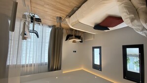 Quarto de hotel moderno com teto de madeira, cama com roupa de cama branca, janela com cortinas e uma pequena mesa com abajur.