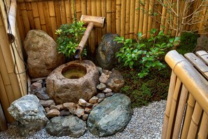 Jardín rocoso con una fuente japonesa tradicional, rodeado de vallas de bambú y follaje.