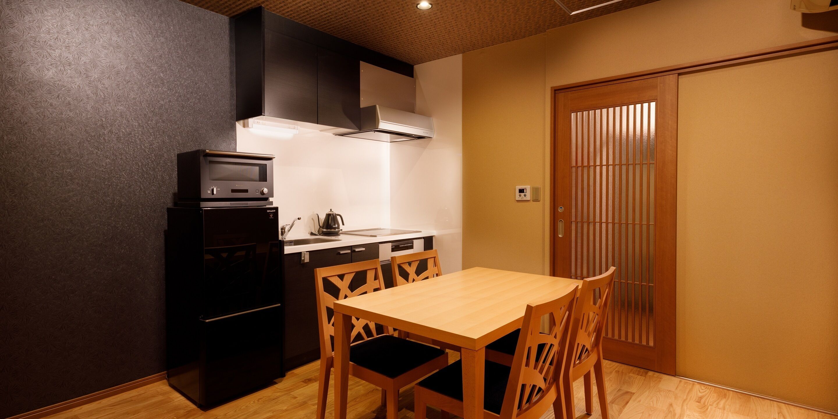 Une cuisine compacte équipée d’un four à micro-ondes, d’une cuisinière et d’un évier. On y trouve une table à manger en bois avec des chaises.