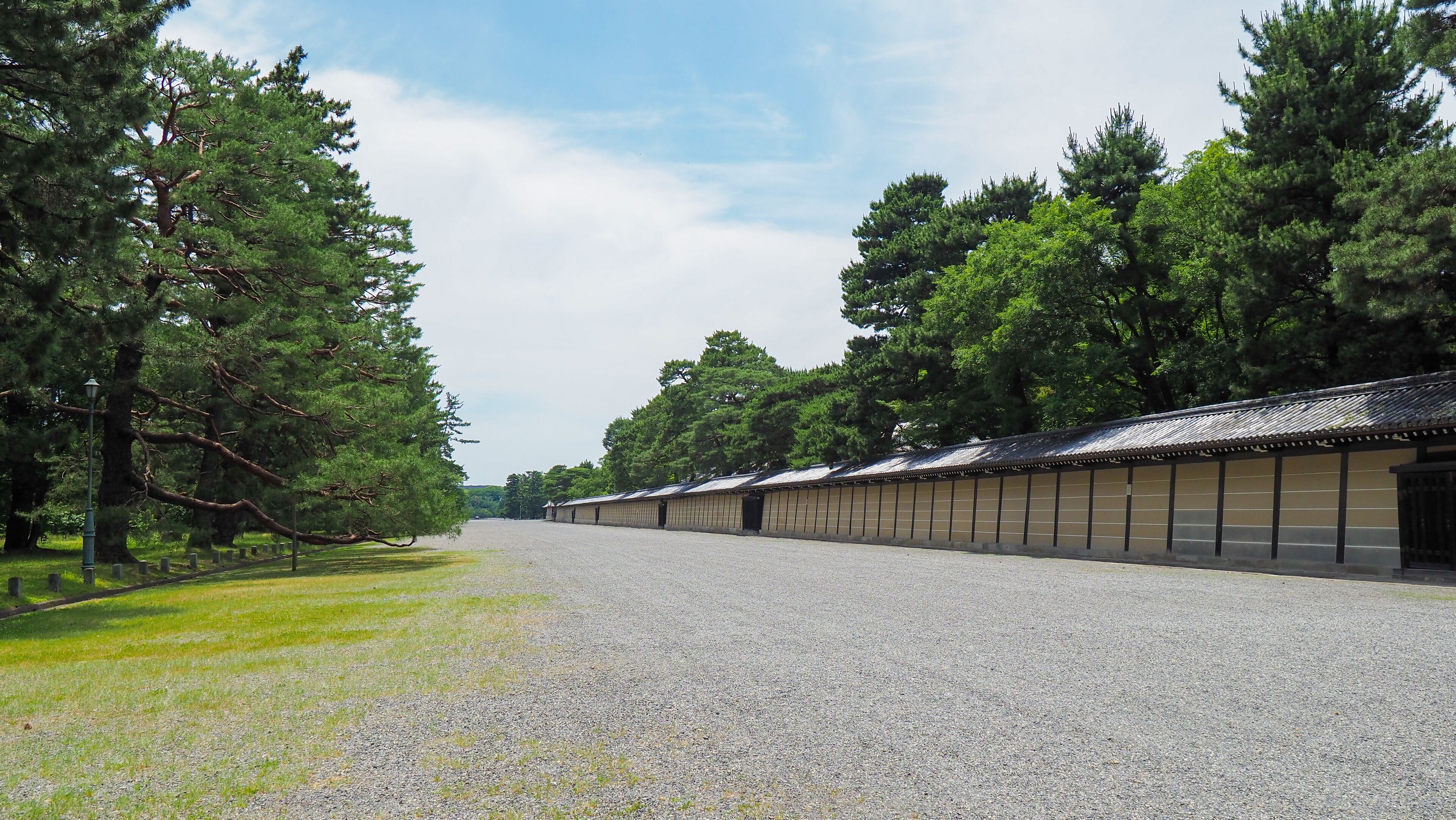 A long building with a traditional roof, surrounded by trees and a gravel path.