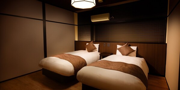 Habitación de hotel con dos camas, cabeceros de madera, una mesita de noche y aire acondicionado instalado en la pared.