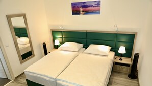 Ein Doppelbett mit grünem Kopfteil, zwei Nachttische mit Lampen, ein Spiegel und ein Gemälde eines Turms an der Wand.