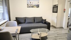 Ein modernes Wohnzimmer mit einem grauen Sofa, einem Glastisch und einem Bild von Heißluftballons an der Wand.