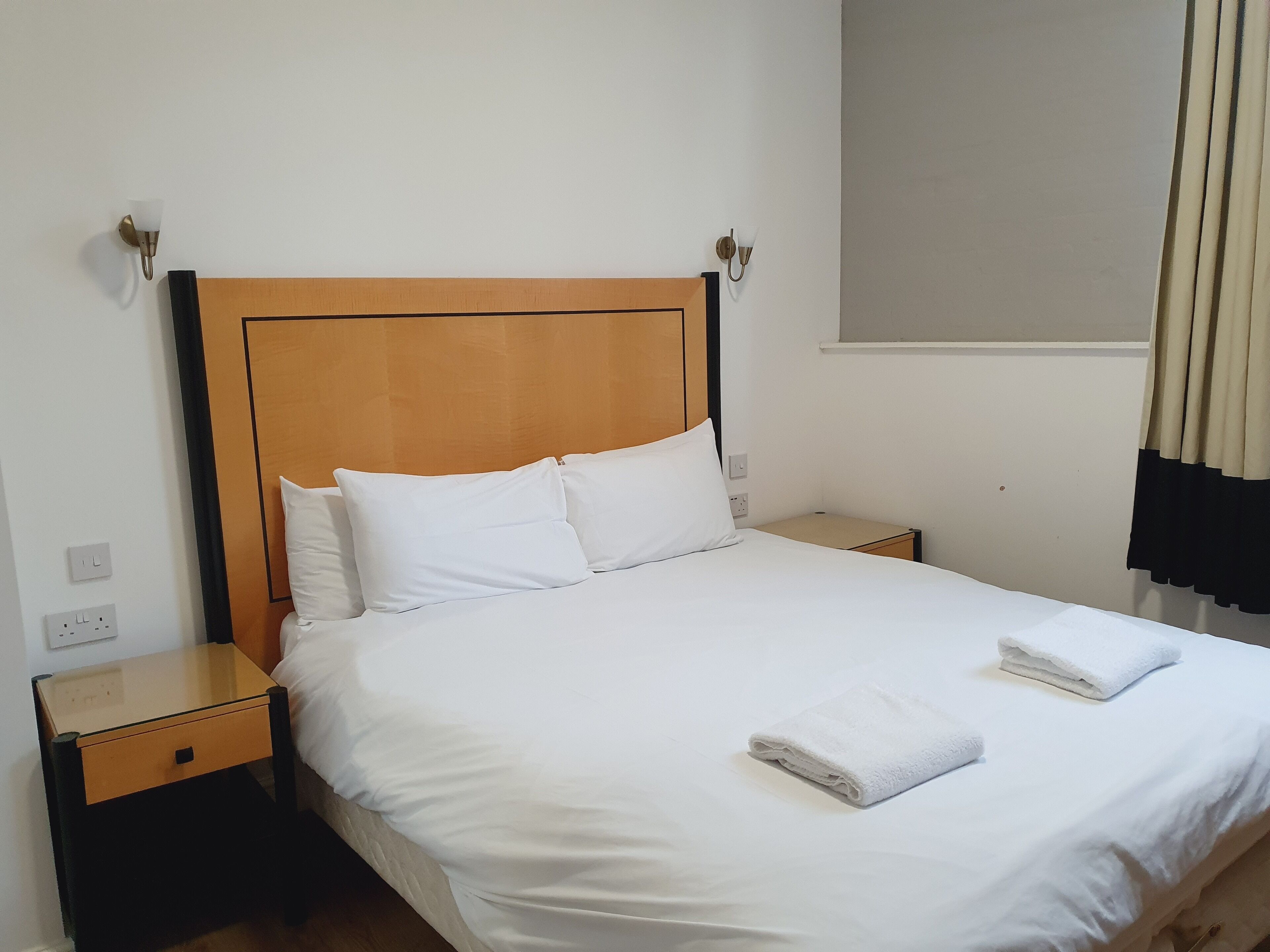 Un lit bien fait, avec du linge de lit blanc, deux tables de chevet et une tête de lit en bois.