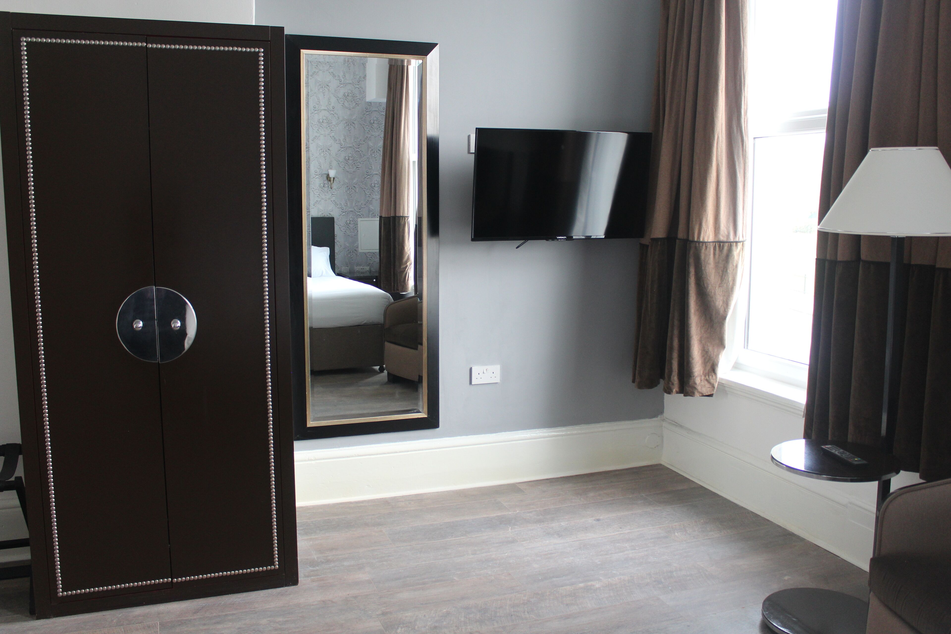 A hotel room with a wardrobe, a bed, a TV, and a window with curtains.