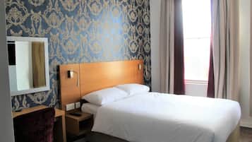 Una camera d'albergo con un letto, una scrivania, una sedia, uno specchio e una finestra con tende.