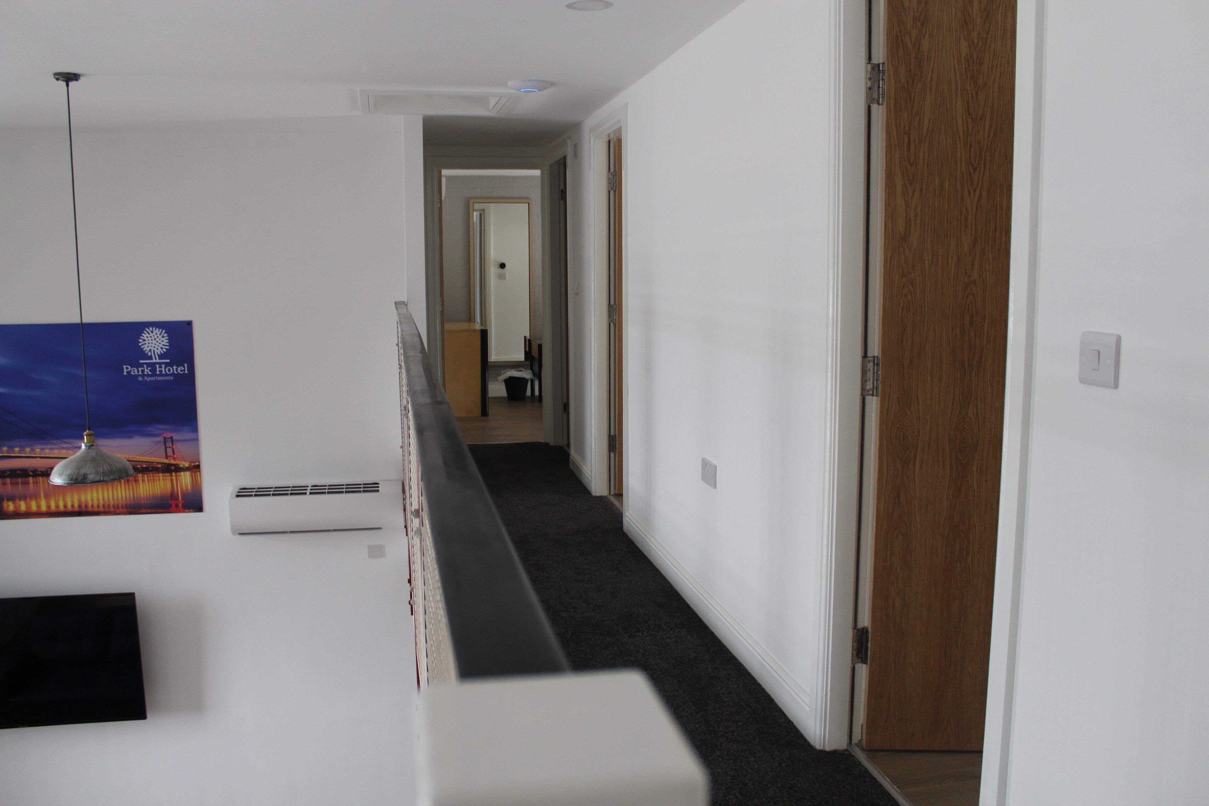 Un couloir d’hôtel avec une affiche représentant un pont, un luminaire au plafond et une porte en bois.