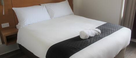 A neatly made bed with white linens, a black bedspread, and a single white towel on the bed.