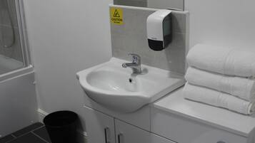 Un baño con lavamanos, espejo, dispensador de toallas y retrete.
