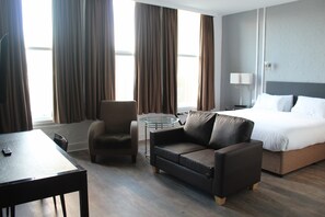 A hotel room with a bed, a sofa, a chair, a small round table, and a desk with a remote control. - Park Hotel & Apartments (Hull)