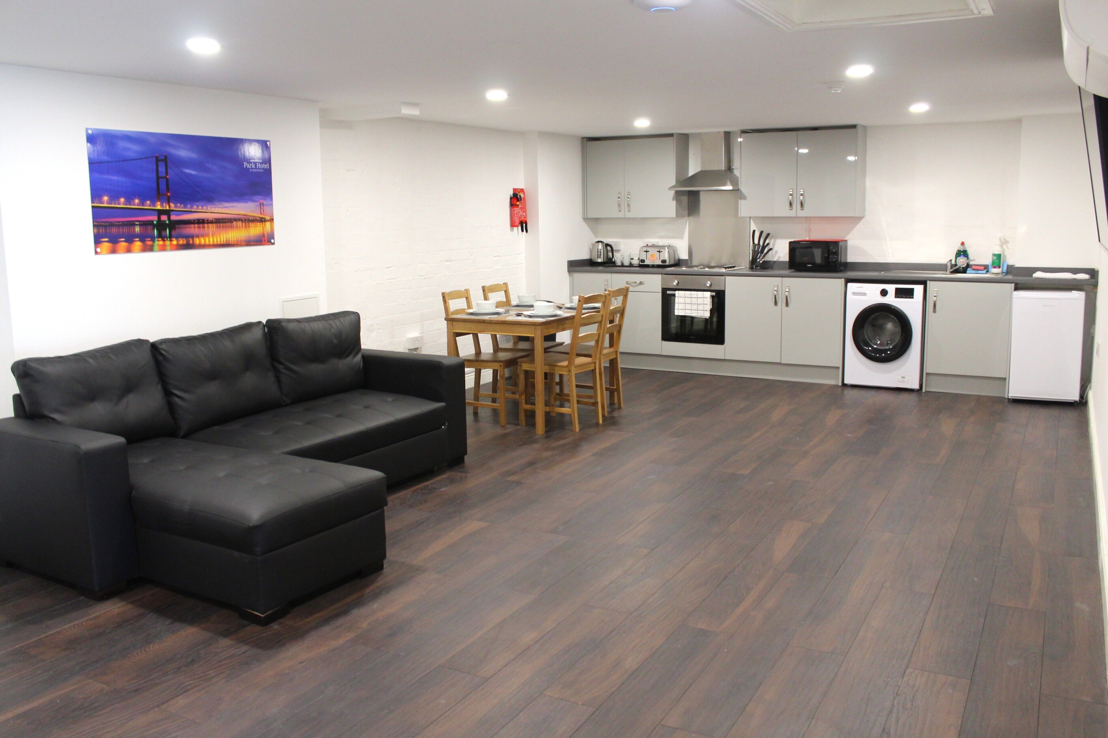 Una sala de estar moderna con un sofá de cuero negro, una mesa de comedor con sillas, una cocina con electrodomésticos y un cuadro en la pared.