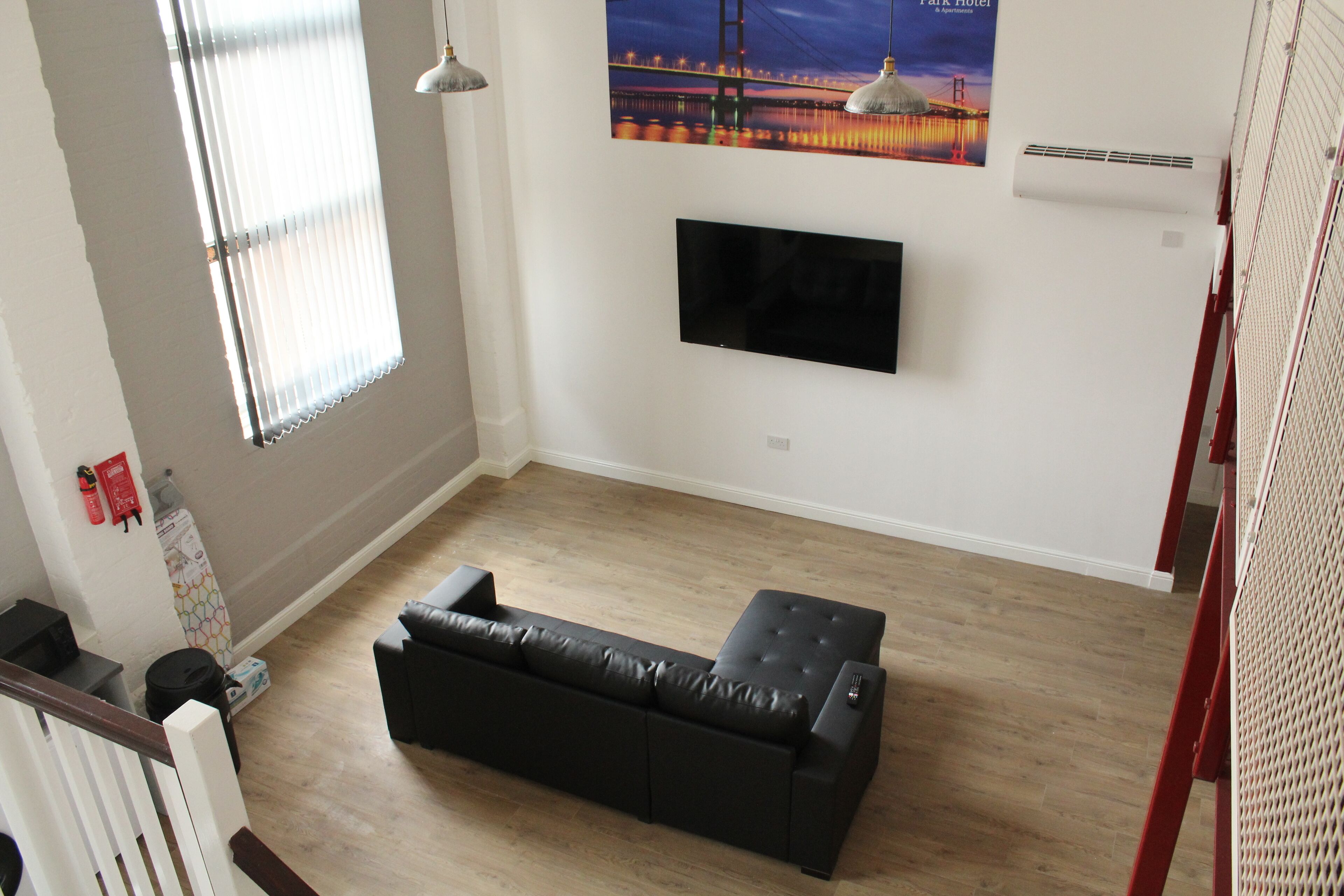 Een moderne woonkamer met een zwarte leren bank, een flatscreen televisie aan de wand en een raam met jaloezieën.